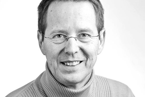 Gesicht eines sympathisch lächelnden Mannes mittleren Alters mit kurzen dunklen Haaren und Brille