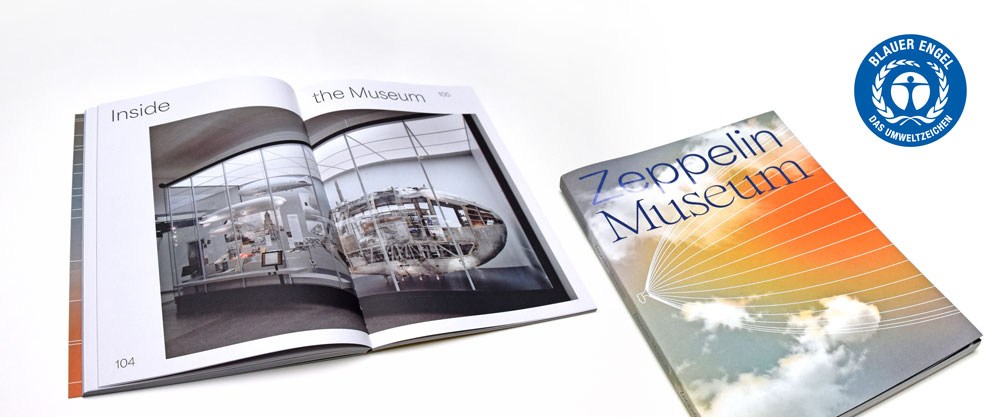 Produktbeispiele Blauer Engel mit einem aufgeschlagenem Magazin mit dem Bild eines Zeppelin