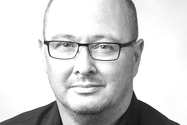 Gesicht eines sympathisch lächelnden Mannes mittleren Alters mit grauem, schütterem Haar